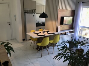 A modern kitchen with a built-in refrigerator, a dining table with yellow chairs, and a large window with a view of the outside. - Apartamento Próximo ao Beto Carrero (Praia de Armação do Itapocorói Penha)