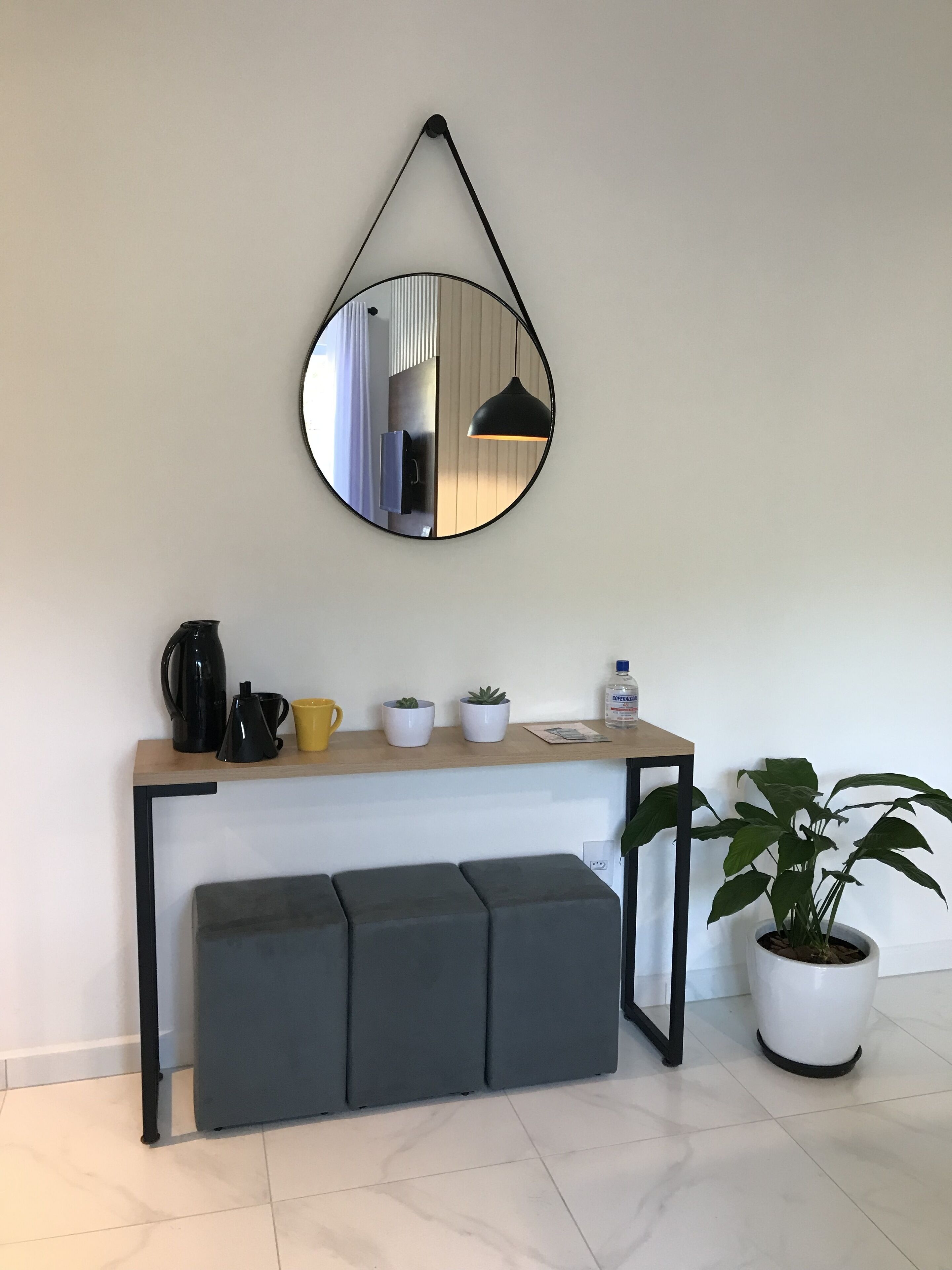A modern kitchenette with a hanging mirror, a coffee maker, a kettle, a yellow mug, and a potted plant.
