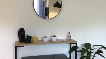 A modern kitchenette with a hanging mirror, a coffee maker, a kettle, a yellow mug, and a potted plant.