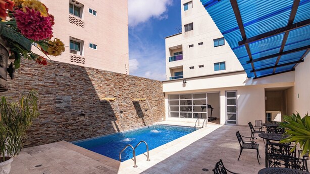 Un espace piscine aménagé sur le toit, avec un mur en pierre, un auvent bleu et du mobilier d’extérieur.