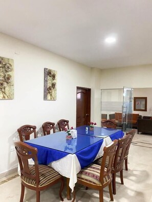 A dining area with a large table covered in blue, surrounded by wooden chairs with cushioned seats. There are two wall-mounted floral paintings above the table. - Hotel Continental Plaza (Barranquilla)