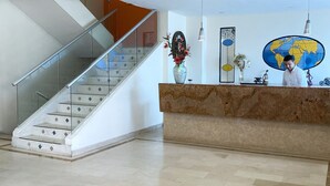 Un hall d’entrée moderne avec un comptoir de réception en marbre, un escalier en verre et un motif décoratif sur le sol.