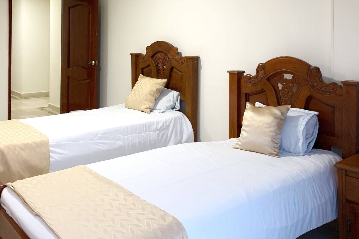 Ein Hotelzimmer mit zwei Einzelbetten, Holz-Kopfteilen und einer Tür zu einem anderen Raum.