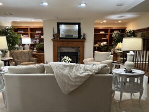 A cozy living room with a fireplace, comfortable seating, and a bookshelf filled with books and decorative items.