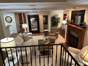 A living room with a sofa, armchairs, a coffee table, and a fireplace. There is a mirror, a lamp, and a clock on the wall.