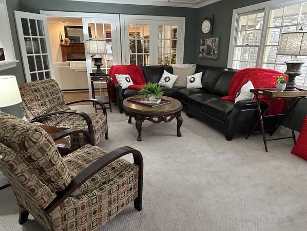 A living room with a black leather sofa, patterned armchairs, a wooden coffee table, and a red throw blanket.