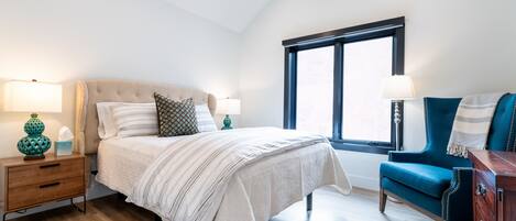 Een slaapkamer met een bed, nachtkastjes, een stoel en een raam.