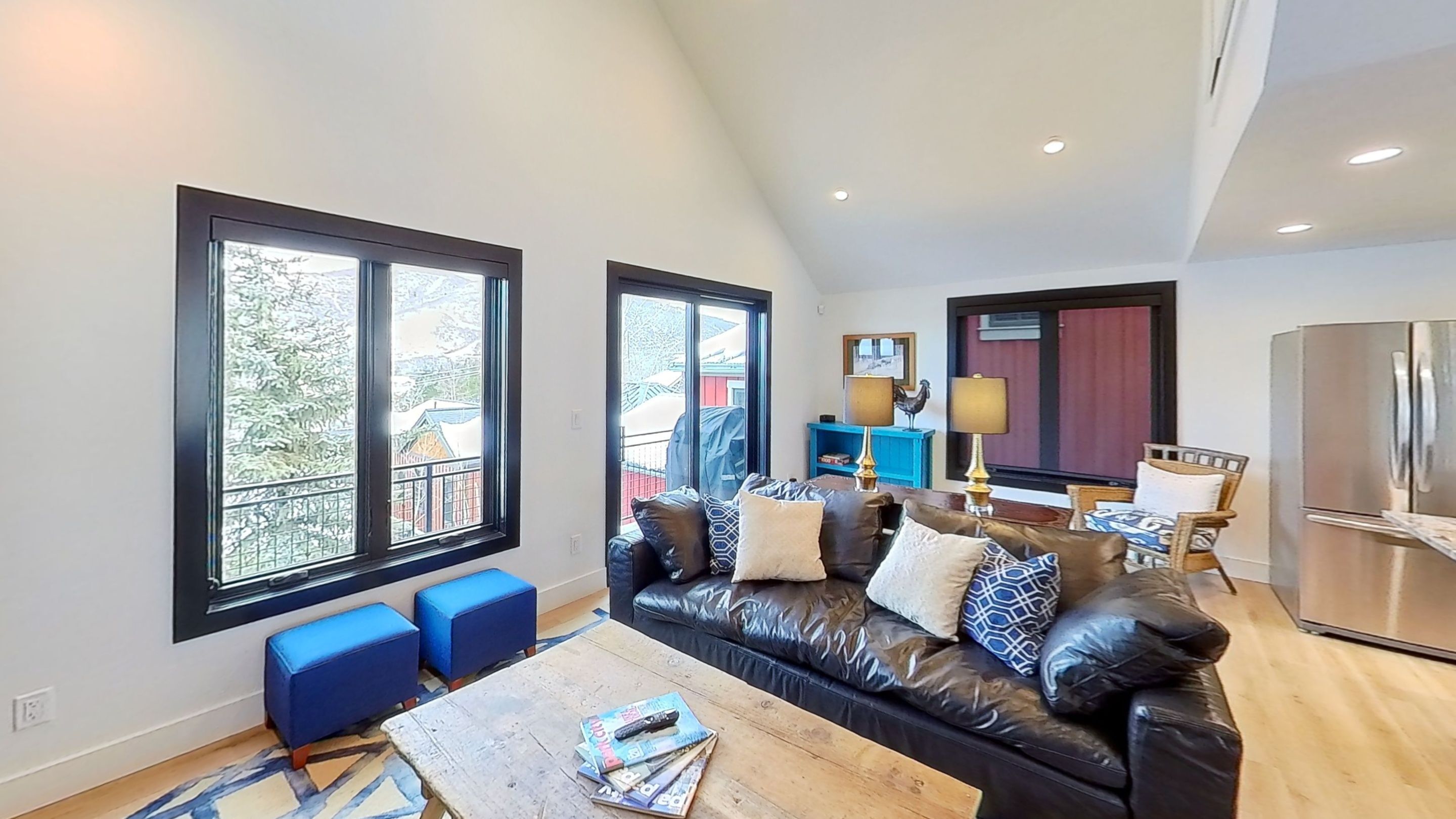 Uma sala de estar moderna com um sofá de couro preto, pufes azuis e uma mesa de centro de madeira.
