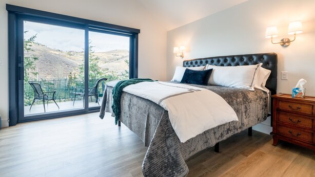 Ein Schlafzimmer mit einer großen Schiebeglasdoor zum Balkon, einem Bett mit einer gepolsterten Kopfstütze und zwei Wandlampen.