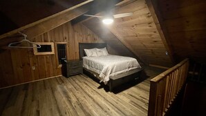 Un dormitorio en un ático de madera con cama, mesita de noche y una lámpara colgante.