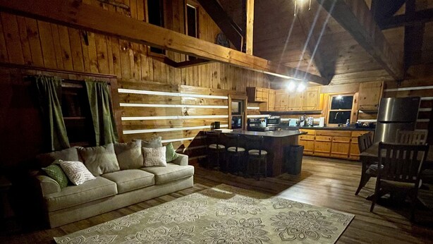 Interior acogedor de una cabaña con techo de madera, un sofá, un tapete estampado y una zona de cocina.