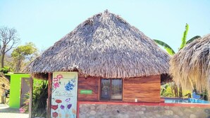 A thatched-roof hut with a stone wall, a colorful flower mural, and a sign reading "La Doyna". - Happy Hill (Chimo)