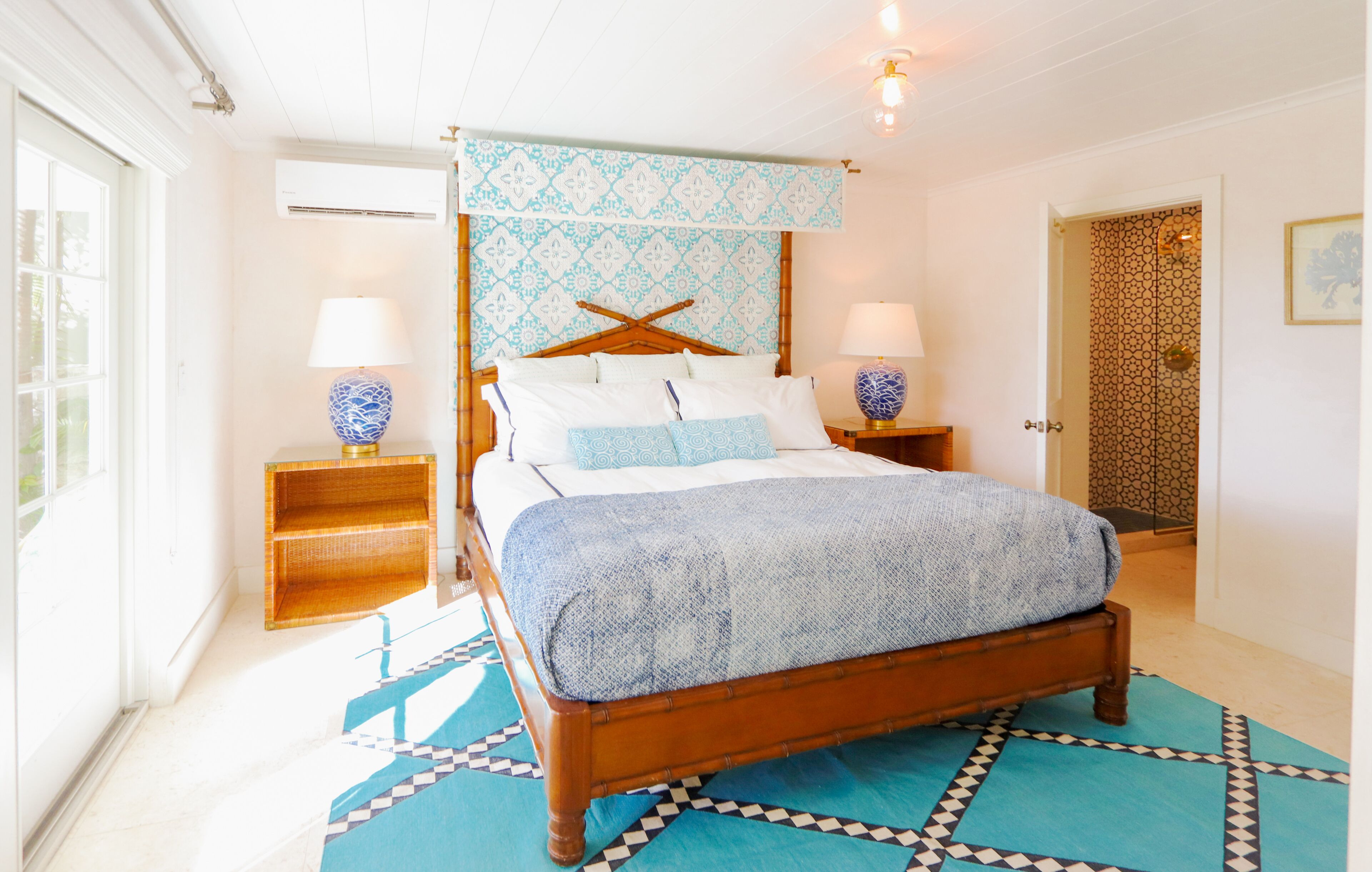 A bedroom with a wooden bed, patterned headboard, two bedside tables with lamps, and a patterned rug.