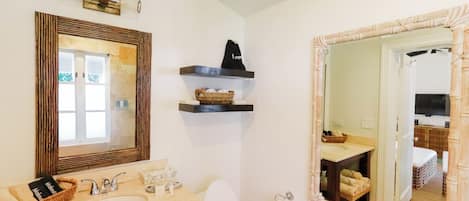 A bathroom with two sinks, a toilet, and a large mirror. There are shelves above the sinks with baskets and a towel.