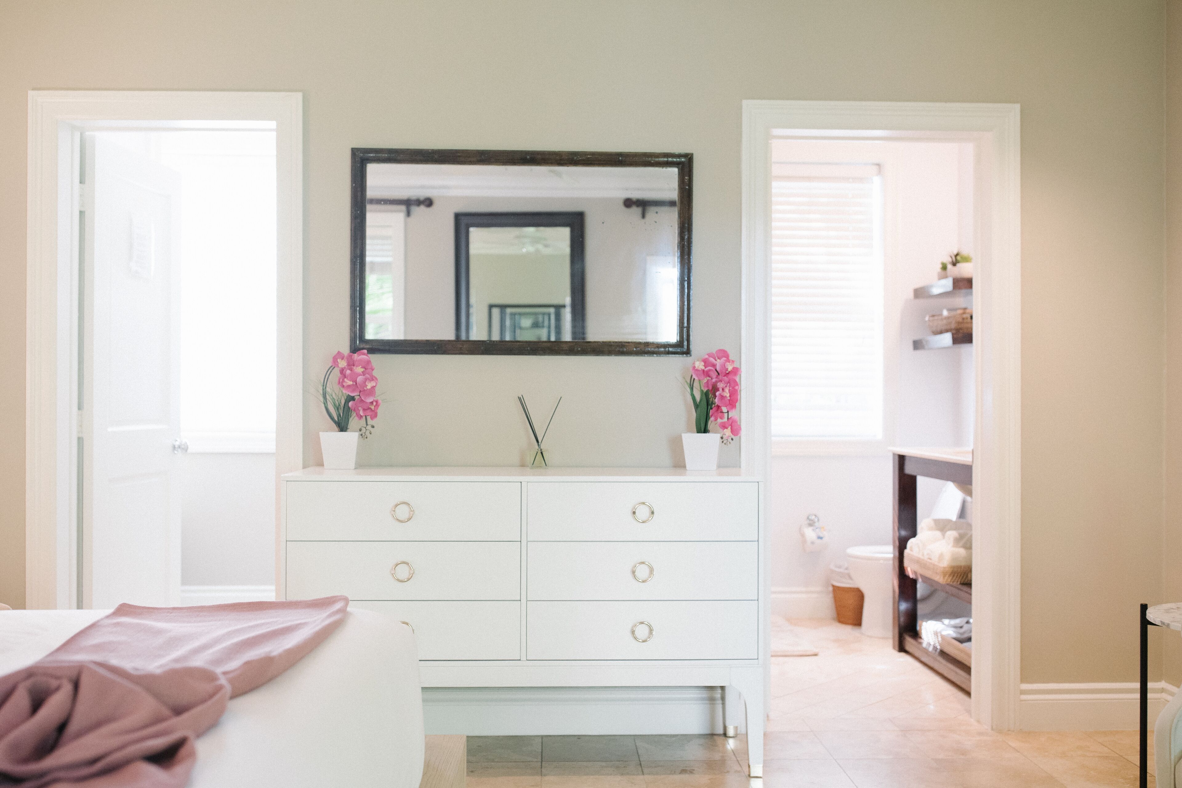 A bathroom with a white vanity, a large mirror, and pink flowers.