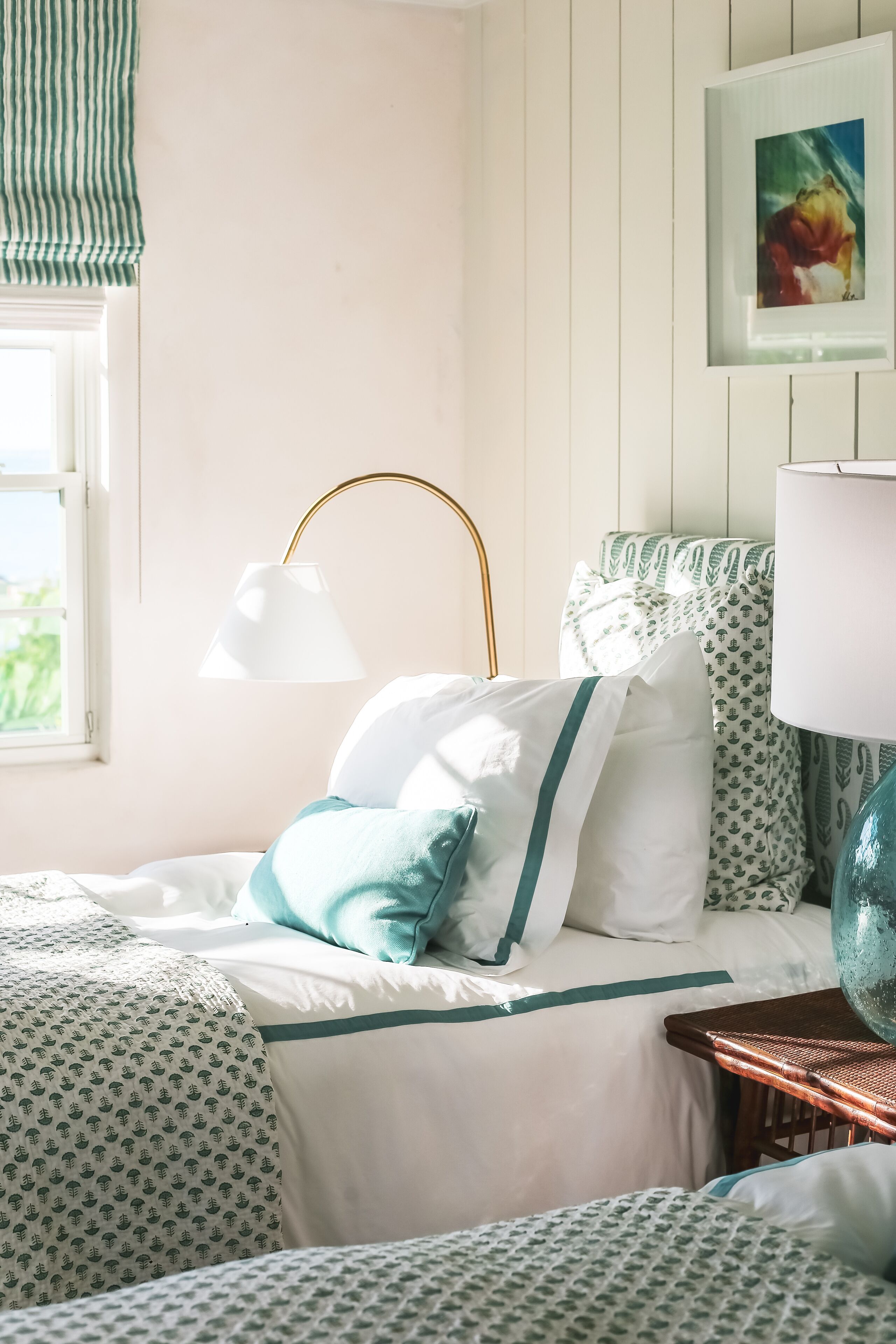 Un dormitorio ordenado con cama, almohadas, lámpara y un cuadro en la pared.