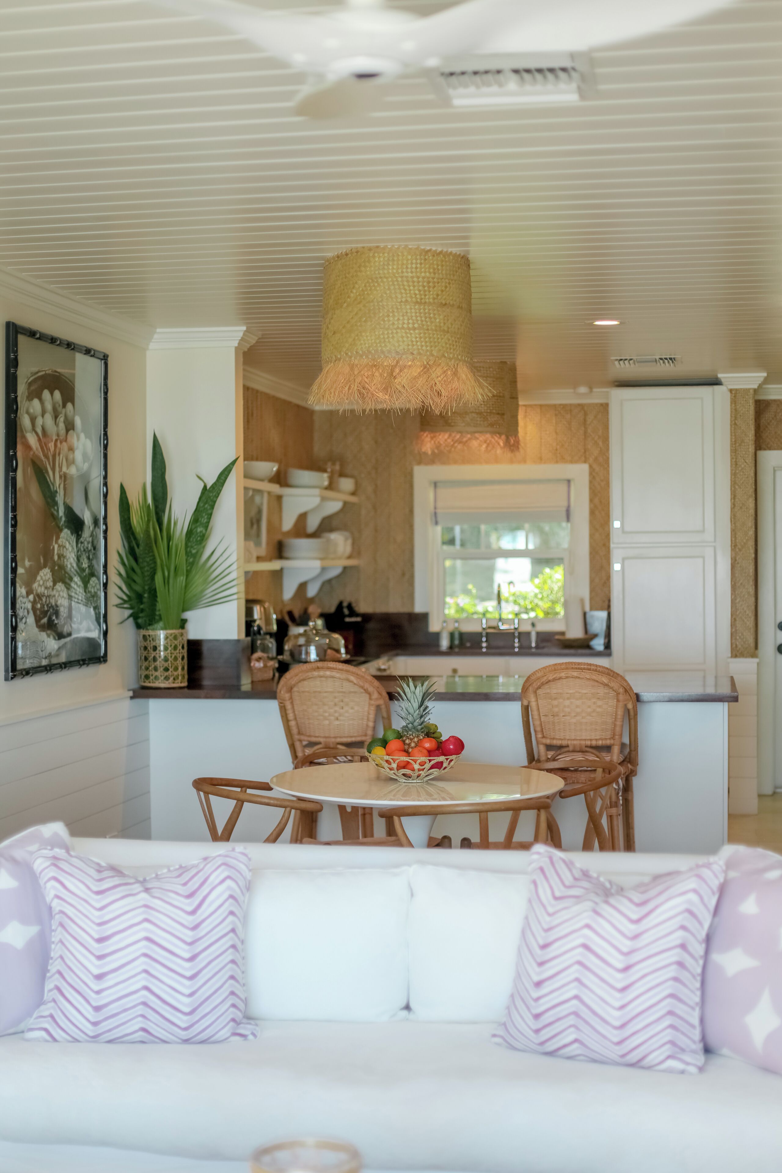 A modern kitchen with white cabinetry, a dining area with wicker chairs, and a large window providing natural light.