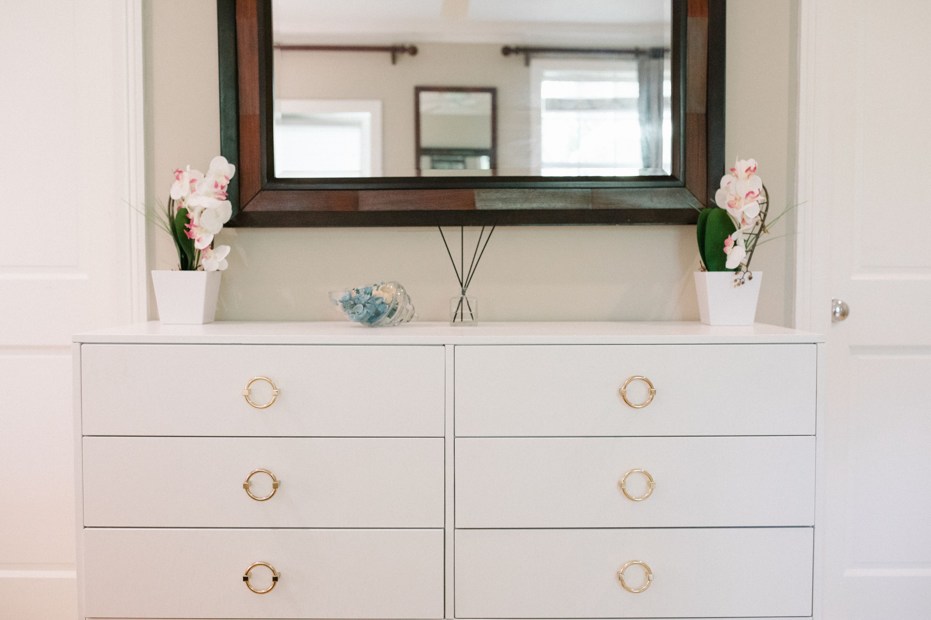 A white dresser with gold circular handles and a mirror above it.