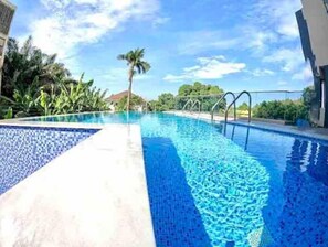 Une piscine à l’eau d’un bleu limpide, entourée de verdure et sous un ciel dégagé.