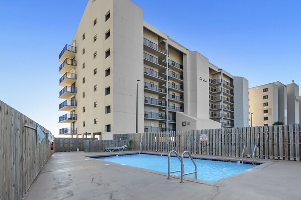 A swimming pool with a wooden fence, a fire hydrant, and a building with multiple balconies.