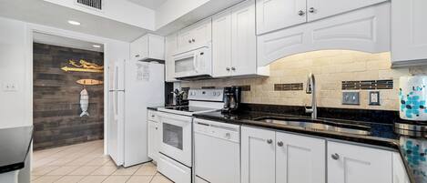 Een moderne keuken met witte kasten, een zwart aanrecht en een betegelde spatwand.