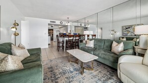 Un salon spacieux avec un canapé vert, une table basse blanche et un coin repas à l’arrière-plan.