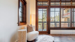 A cozy room with a white sofa, a fluffy rug, a tall lamp, and a large window with a view of trees and buildings. - Luxury Resort Living, Private Hot tub with 2 Master BD (Park City)