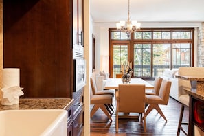 A dining area with a table and chairs, a chandelier, and a large window with a view of trees. - Luxury Resort Living, Private Hot tub with 2 Master BD (Park City)
