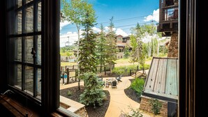 A view through a window of a courtyard with a patio, outdoor seating, and a stone building. - Luxury Resort Living, Private Hot tub with 2 Master BD (Park City)