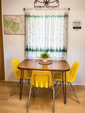 A dining area with a wooden table, yellow chairs, a map on the wall, and a curtain with a forest pattern. - Quiet Escape for Hunters & Family Retreats! (Alpine)