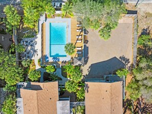 An aerial view of a resort with a swimming pool, lounge chairs, and palm trees.