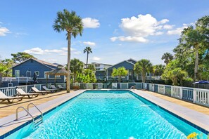 A swimming pool with lounge chairs and palm trees, surrounded by buildings with balconies.