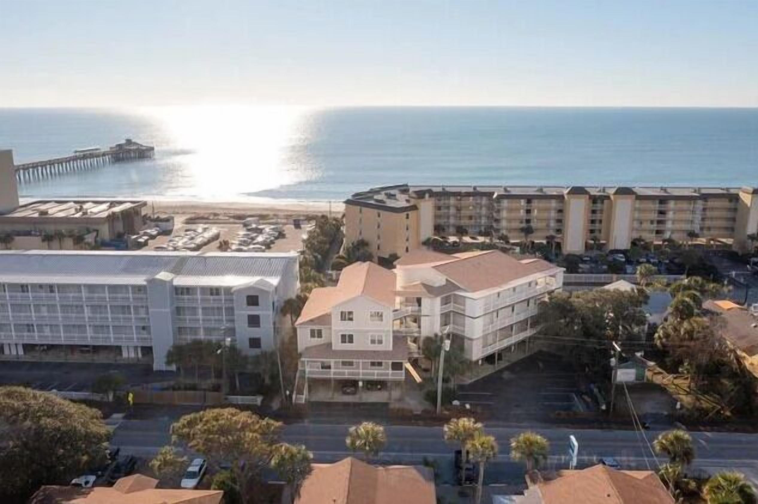 Un hotel costero con varias construcciones, un estacionamiento y un muelle al fondo.