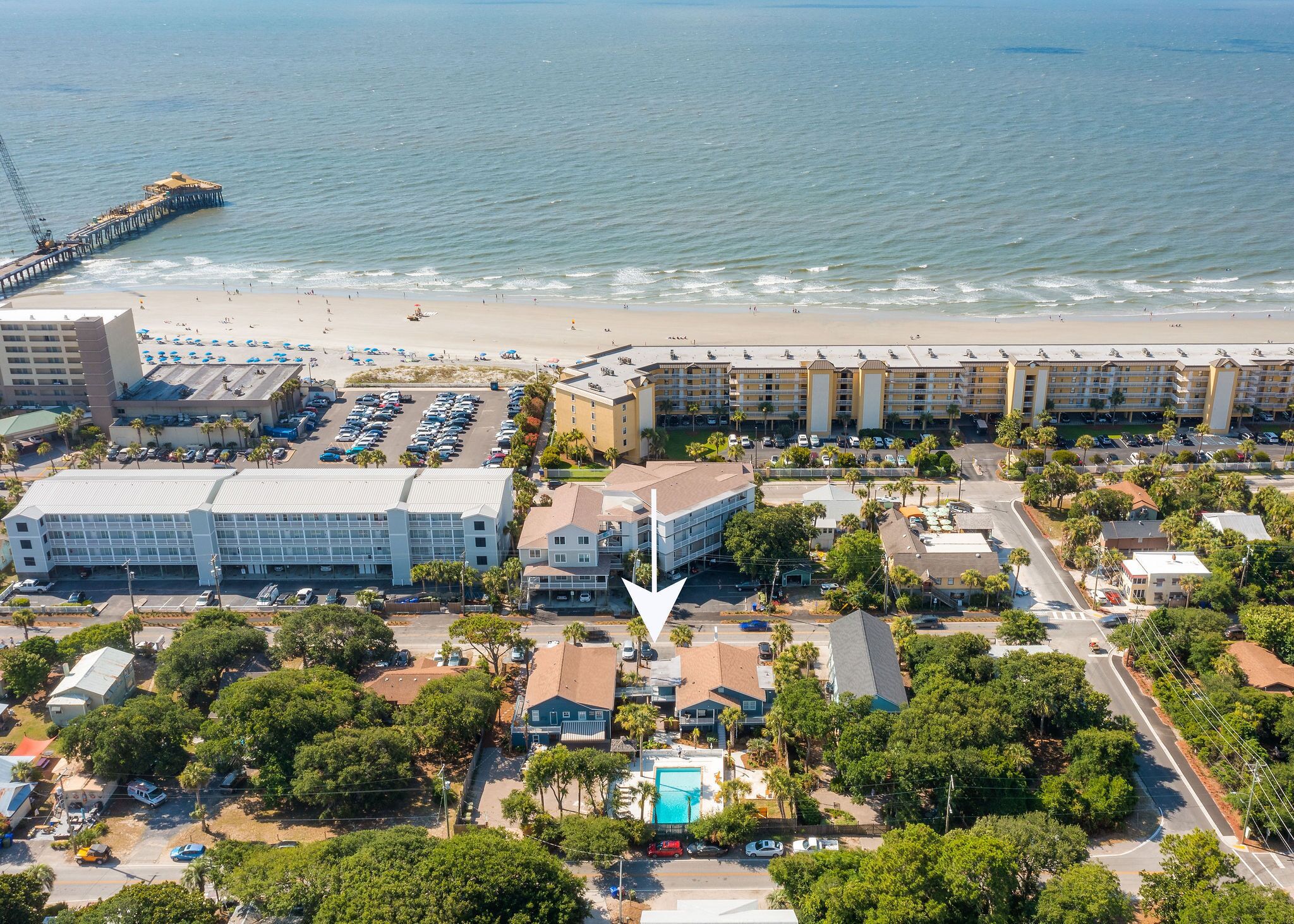 Luftaufnahme einer Küstenhotelanlage mit mehreren Gebäuden, einem Strand und einem Steg.