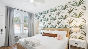 A hotel room with a large bed, a nightstand, a lamp, and a window with curtains. - Folliday Inn - The Racer - Room 35 (Folly Beach)