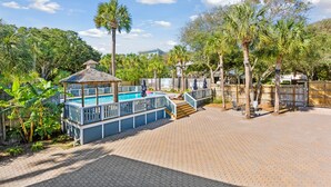 A pool area with a gazebo, palm trees, and a brick patio. - Folliday Inn - The Racer - Room 35 (Folly Beach)