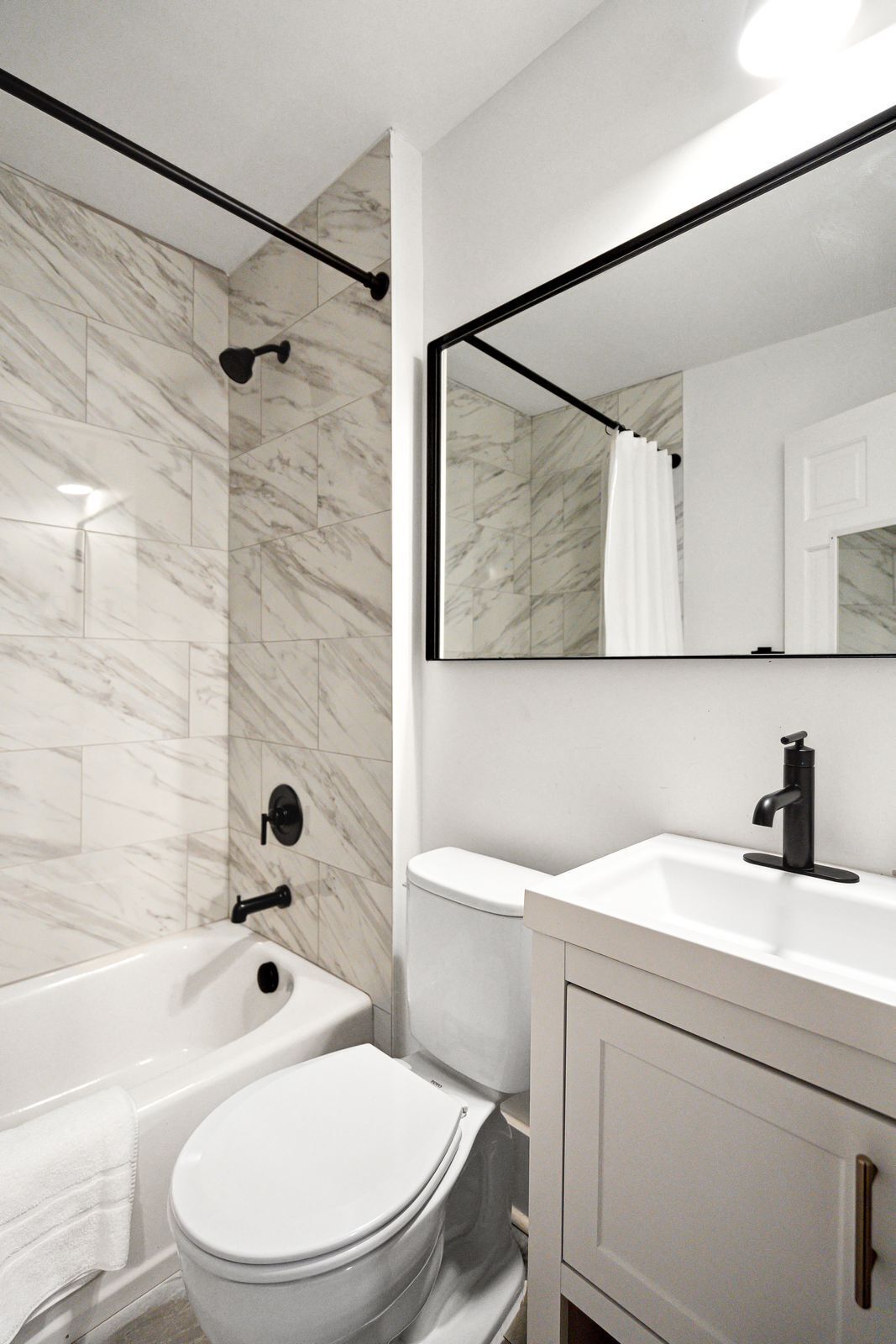 A modern bathroom with a white toilet, a bathtub, and a sink with a mirror above.