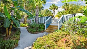 A pathway leading to a wooden staircase with a blue railing, surrounded by lush greenery and palm trees. - Folliday Inn - The Coronado - Room 11 (Folly Beach)