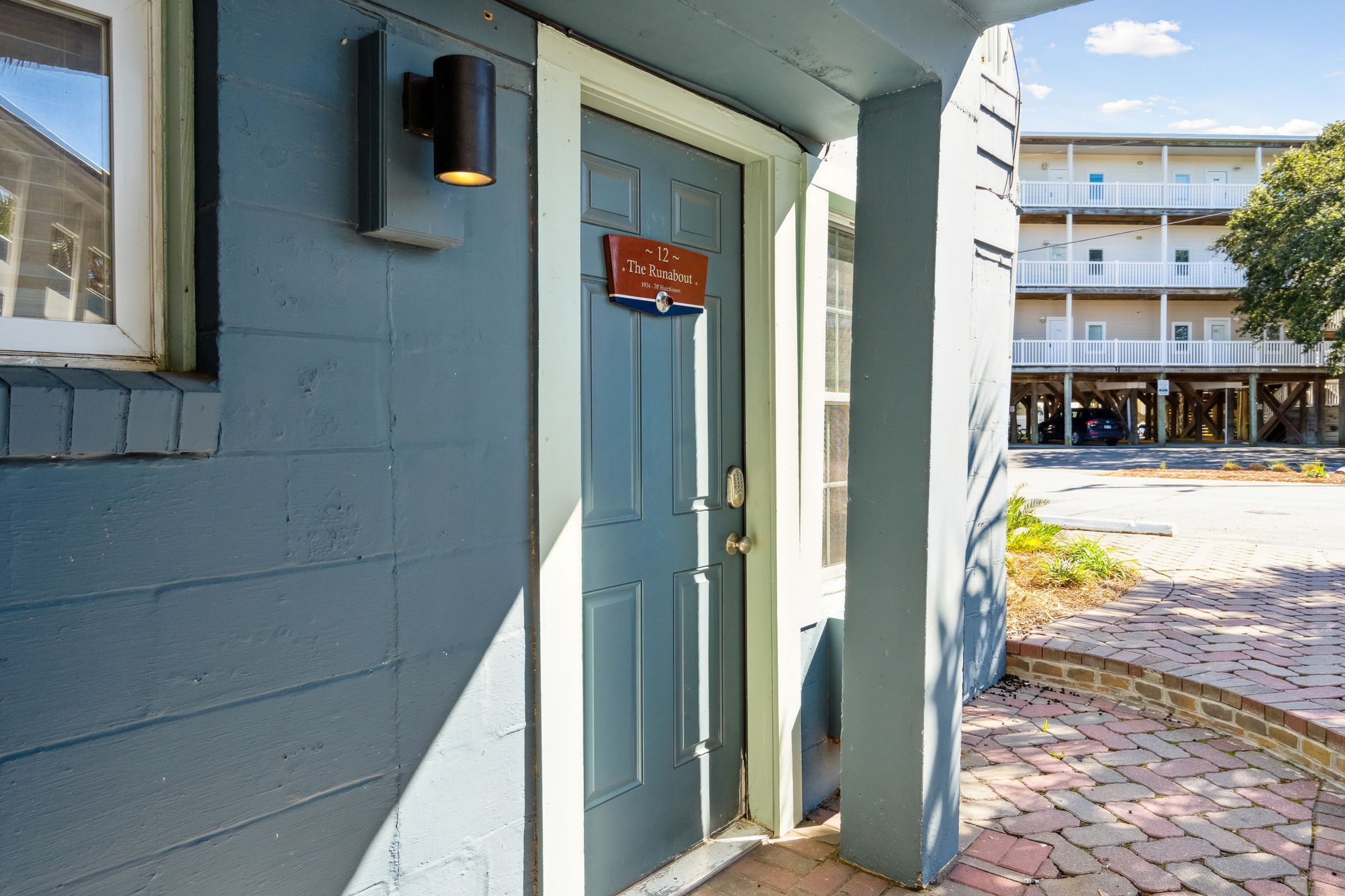 A building with a blue exterior, a door with a sign, and a brick pathway leading to a parking area.