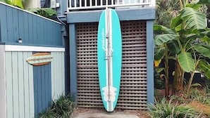 A turquoise surfboard leaning against a blue gate with a decorative sign. - Folliday Inn: Room: The Dolphin: Room 36 (Folly Beach)