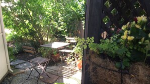 A garden patio with a table and chairs, surrounded by potted plants and a wooden fence.