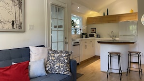 A modern kitchen with a built-in oven, microwave, and refrigerator. There is a dining area with a bar stool and a sofa with patterned cushions.