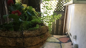 A garden area with a hanging planter filled with plants and flowers, a stone pathway, and a wooden gate.