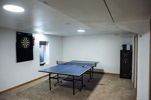 A room with two ping pong tables, a dartboard, and a small window. - Platte River Cabin @ Pine -Main (Pine)