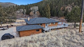 A two-story log cabin with a deck, surrounded by a forested area and a mountain in the background. - Platte River Cabin @ Pine -Main (Pine)
