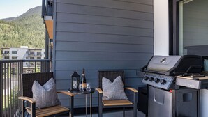 A balcony with two wicker chairs, a small table with a bottle and glasses, and a portable grill. - Farwell's Spike by Revelstoke Vacations (Revelstoke)