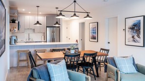 A modern kitchen with a central island, wooden dining table, and chairs. There are pendant lights above the island and a framed picture on the wall. - Farwell's Spike by Revelstoke Vacations (Revelstoke)