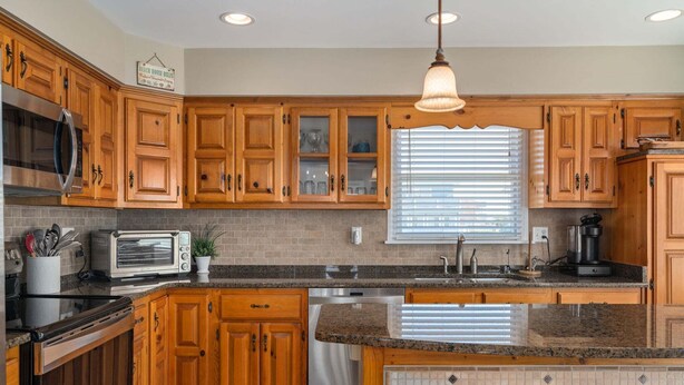 A kitchen with wooden cabinets, a built-in oven, a microwave, a sink, and a window with blinds. - Sunwatch: Soundfront, Hot Tub, Private Boat Dock and Community Pool Access (Nags Head)