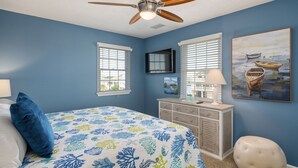 A bedroom with a bed, a dresser, a chair, a ceiling fan, and a painting on the wall. - Sunwatch: Soundfront, Hot Tub, Private Boat Dock and Community Pool Access (Nags Head)