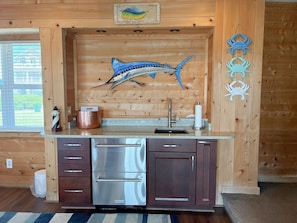 A kitchen with wooden cabinetry, a stainless steel refrigerator, a sink, and decorative crab wall art.